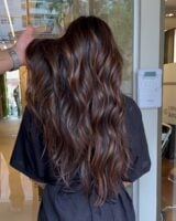 Mulher com cabelo longo, ondulado e com luzes na técnica morena iluminada na cor chocolate