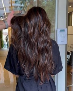 Mulher com cabelo longo, ondulado e com luzes na técnica morena iluminada na cor chocolate