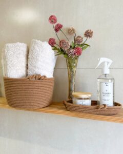 Prateleira de madeira com cesto e bandeja marrom com vaso de flores e toalhas enroladas