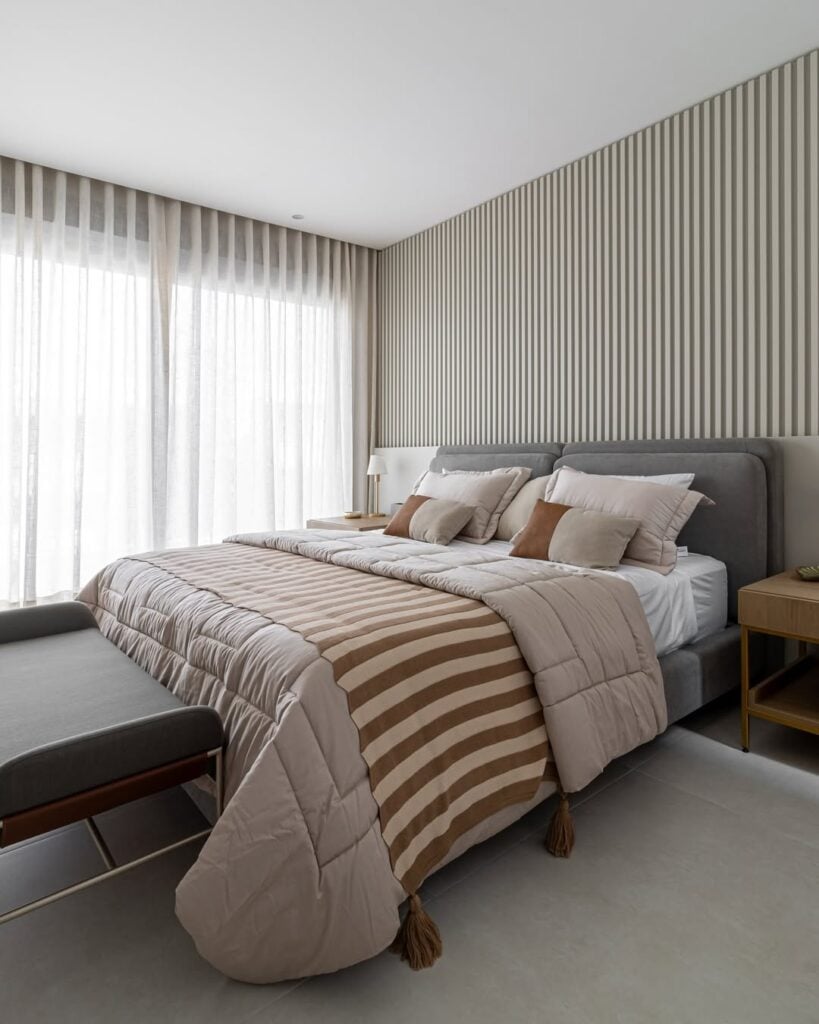 Quarto de casal com cabeceira estofada em veludo cinza e parede revestida com painel ripado