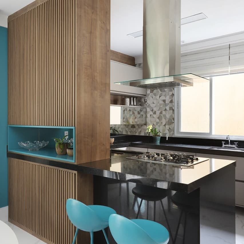 Cozinha com bancada preta, cadeiras azuis e painel ripado com nicho azul