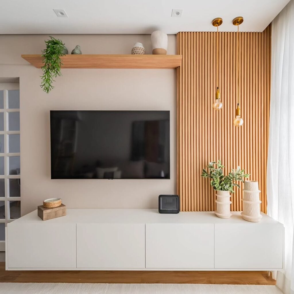 Sala com painel ripado ao lado da tv, prateleira com objetos decorativos e rack branco