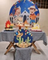 Mesa posta com toalha xadrez em preto e branco, painel com bonecos e igreja