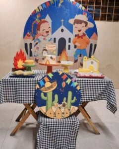 Mesa posta com toalha xadrez em preto e branco, painel com bonecos e igreja