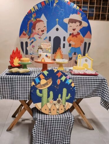 Mesa posta com toalha xadrez em preto e branco, painel com bonecos e igreja