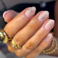 Mão de pele clara, com acessórios em dourado e unha amendoada nude com estrela dourada