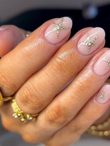 Mão de pele clara, com acessórios em dourado e unha amendoada nude com estrela dourada