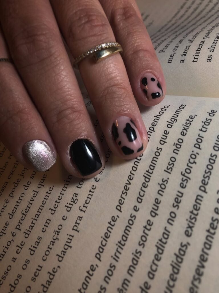 Mão de pele clara, com anel em dourado e unha curta com estampa cow print