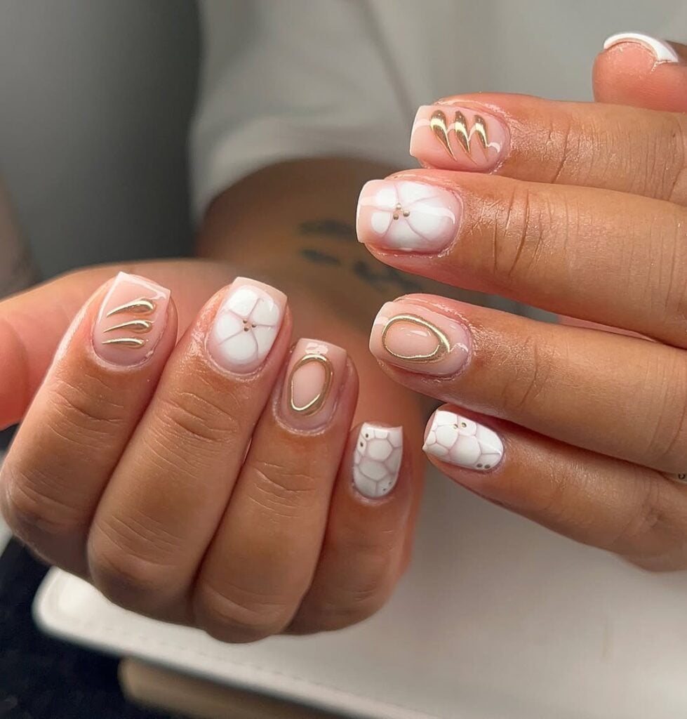 Mãos de pele clara, com unha curta decorada com esmalte branco e gel dourado