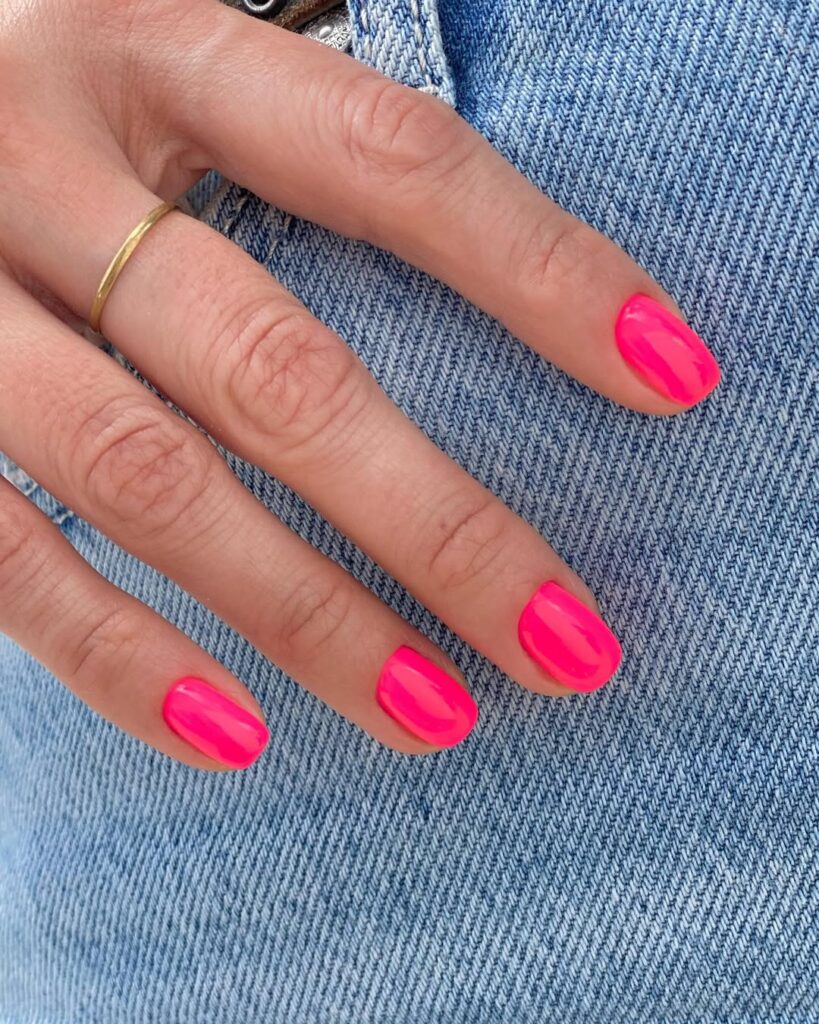 Mão de pele clara, com anel em dourado e unha curta e quadrada hot pink 