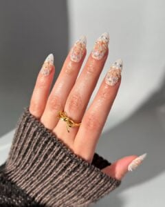 Mão de pele clara, com anel dourado e unha amendoada com design de bolo de aniversário