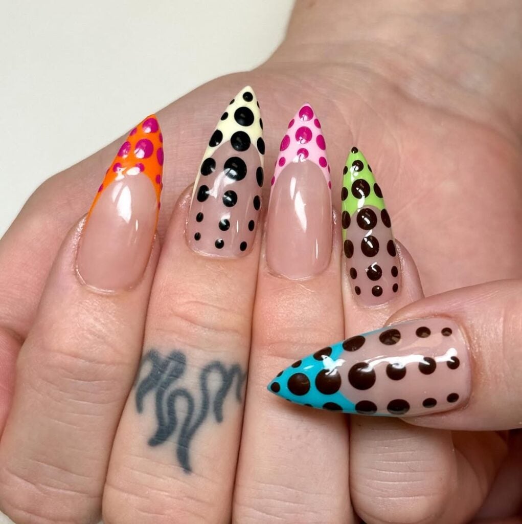 Mão de pele clara, com unha stiletto com inglesinha e poá colorido 