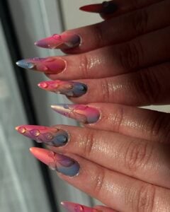 Mão de pele clara, com unha stiletto tie dye com decoração em gel