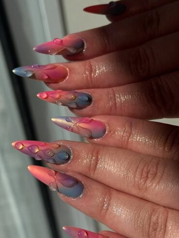 Mão de pele clara, com unha stiletto tie dye com decoração em gel