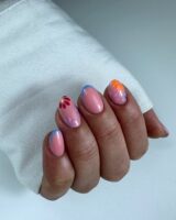 Mão de pele clara, com unha amendoada nude com flores e inglesinha azul-claro
