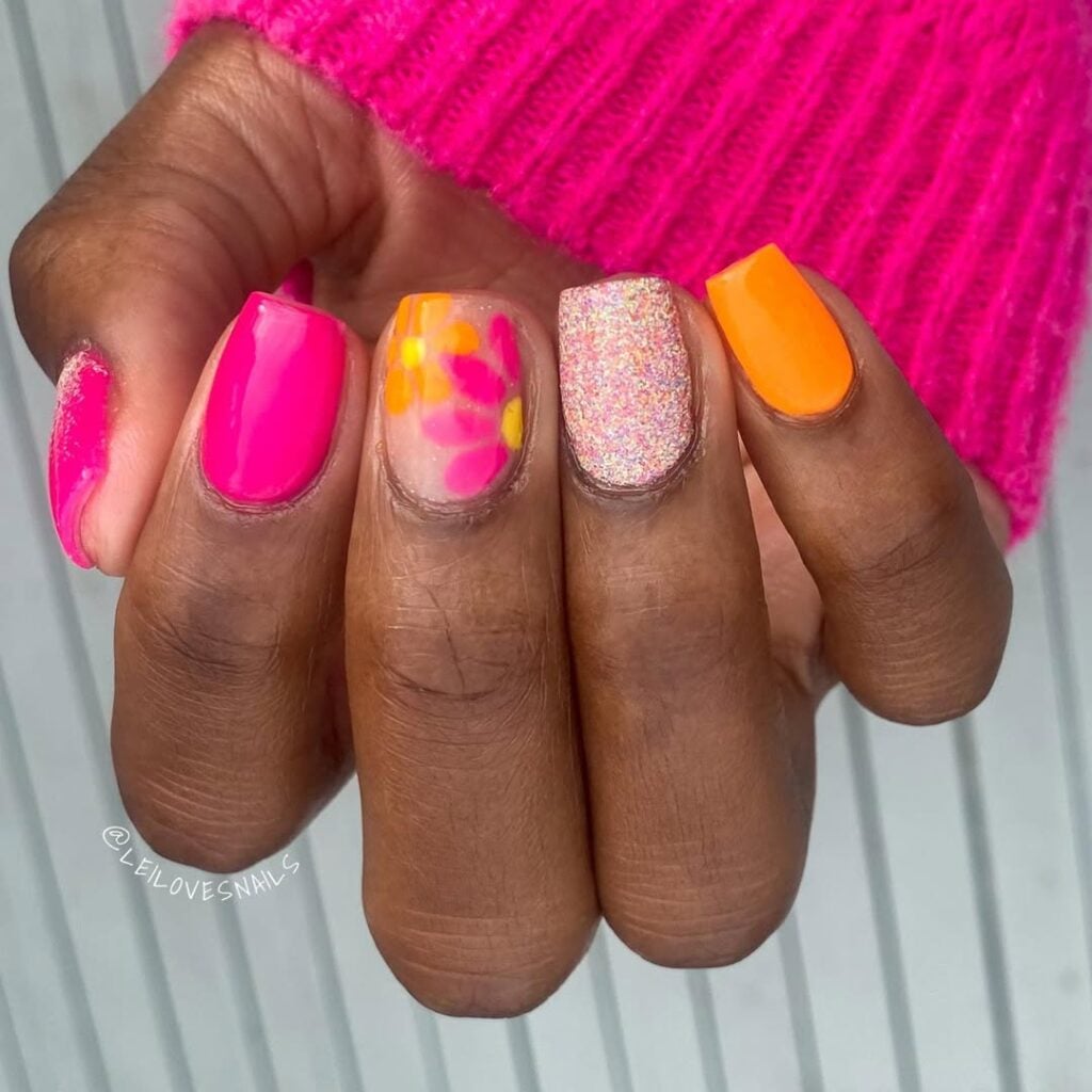 Mão de pele preta, com unha quadrada rosa, laranja, com glitter e flores