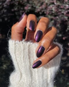 Mão de pele preta, com anel em dourado e unha amendoada com esmalte roxo metalizado
