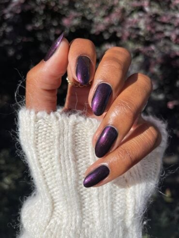 Mão de pele preta, com anel em dourado e unha amendoada com esmalte roxo metalizado