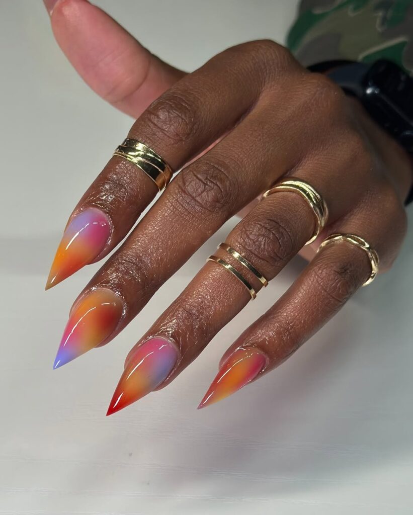 Mão de pele preta, com anéis em dourado e unha stiletto tie dye