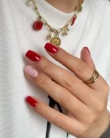 Mão de pele clara, com acessórios em dourado e unha quadrada vermelha com strass