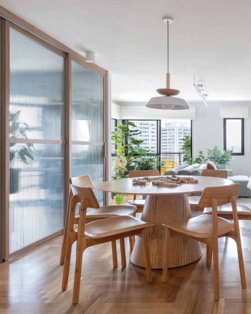 Sala de jantar com mesa e cadeiras de madeira e porta de correr com vidro canelado