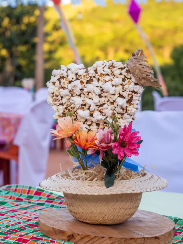 Centro de mesa junino com chapéu de palha, flores e coração coberto com pipocas