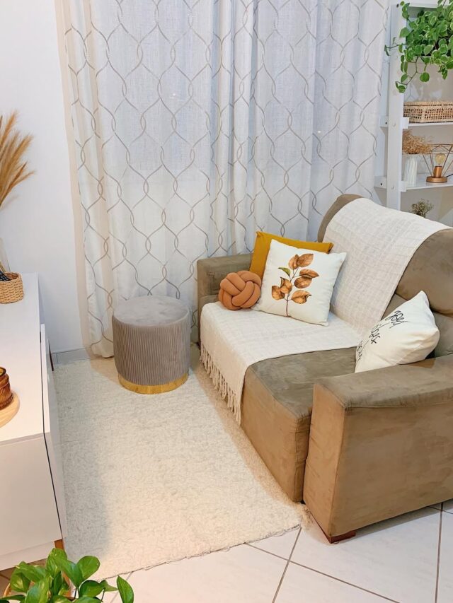 Sala de estar com sofá em fom de marrom claro, com manta crua e almofadas