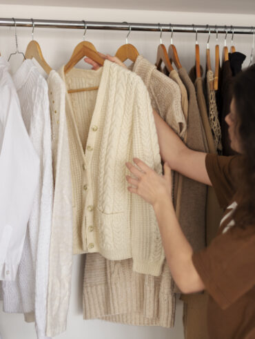 Mulher jovem com cabelos longos castanhos olhando as roupas do roupeiro