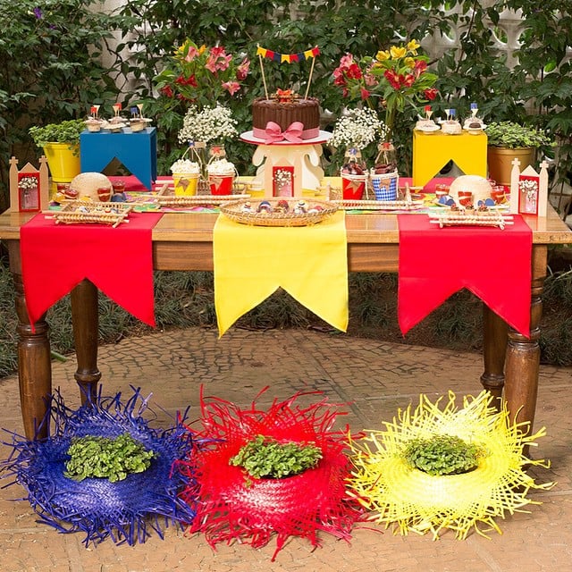 Mesa de madeira com decoração junina, bandeirinhas coloridas, chapéus de palha com plantas