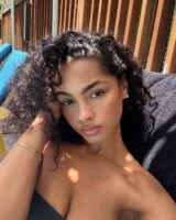 Mulher de pele preta-clara, com acessórios em dourado e cabelo escuro cacheado