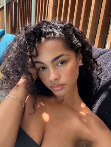 Mulher de pele preta-clara, com acessórios em dourado e cabelo escuro cacheado