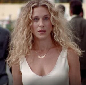 Carrie Bradshaw, com vestido branco e cabelo loiro cacheado