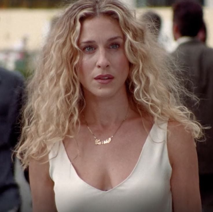 Carrie Bradshaw, com vestido branco e cabelo loiro cacheado