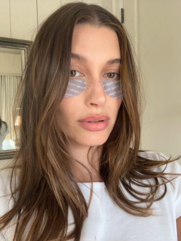 Hailey Bieber, com blusa branca, cabelo castanho e patches na área dos olhos