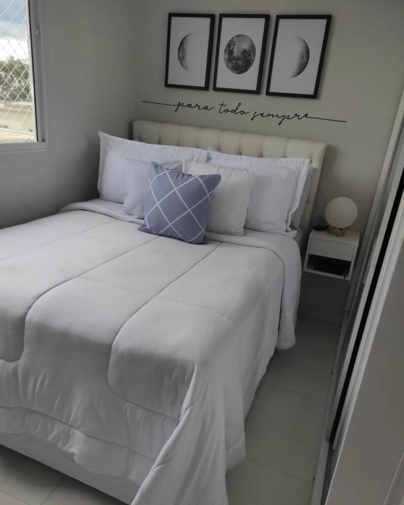 Quarto com cabeceira estofada capitonê, roupa de cama branca e uma almofada cinza