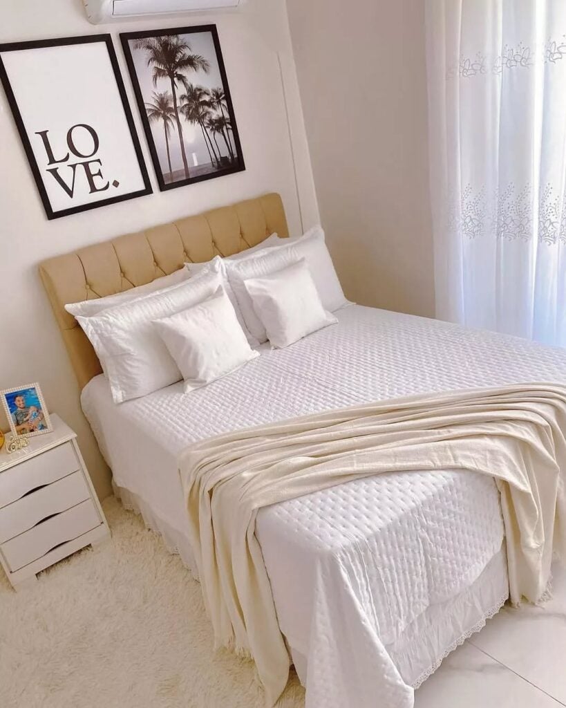 Quarto com cabeceira capitonê bege, lençol e colcha branca com manta bege