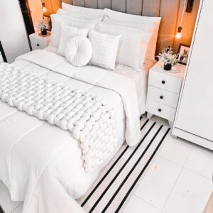Quarto de casal com cama postra branca com várias almofadas, colcha e manta
