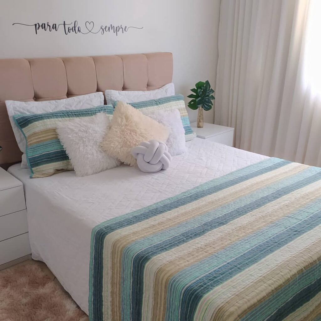 Cama com cabeceira rose aveludada, roupa de cama branca, azul e bege
