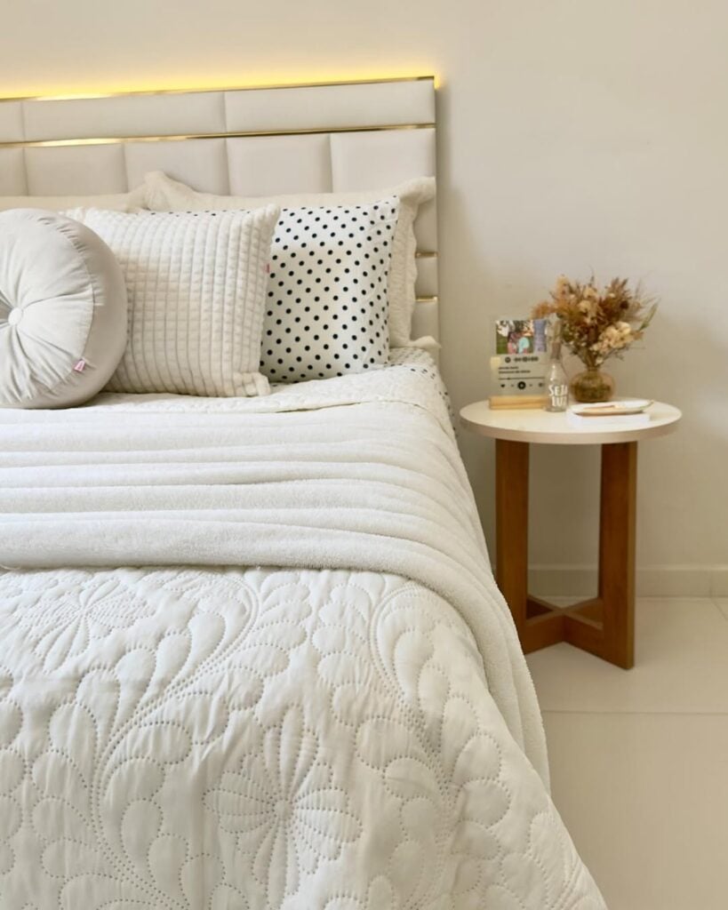 Cama posta branca com mesinha de cabeceira redonda e objetos decorativos
