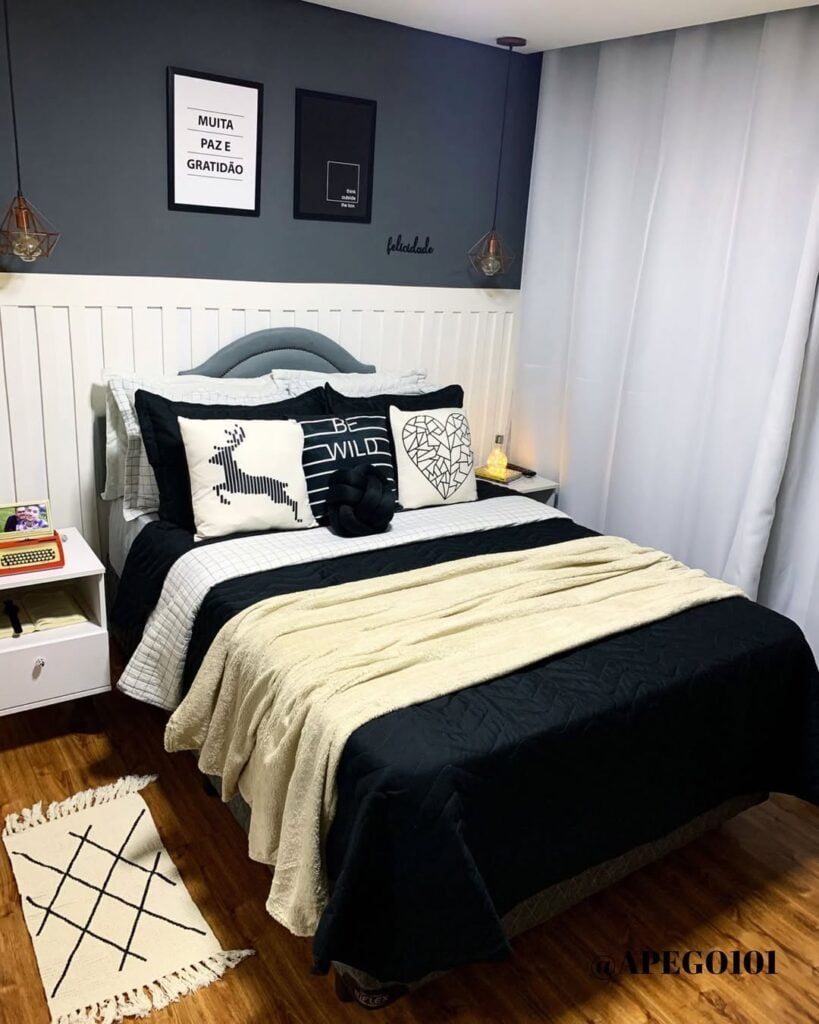 Quarto com parede cinza, cabeceira em lambri branco e cama posta preta com várias almofadas