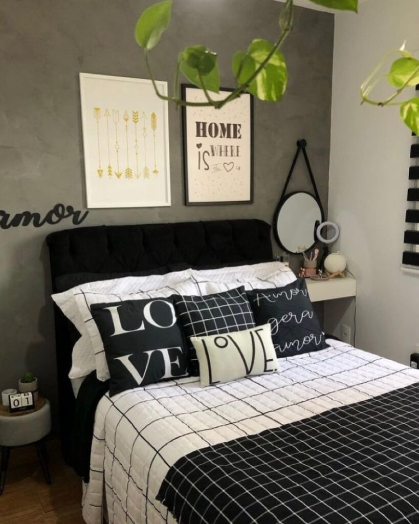 Quarto com parede cinza com quadros, cabeceira em veludo preta e cama posta em preto e branco