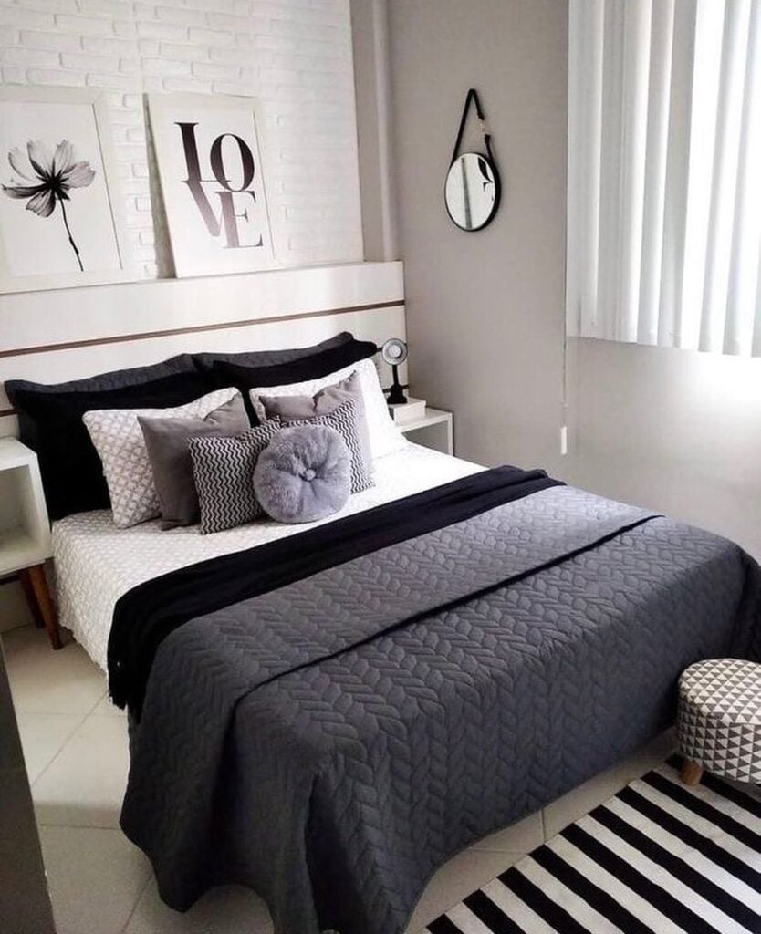 Quarto com paredes brancas, quadros, cama posta em preto, branco e cinza e tapete listrado em branco e preto