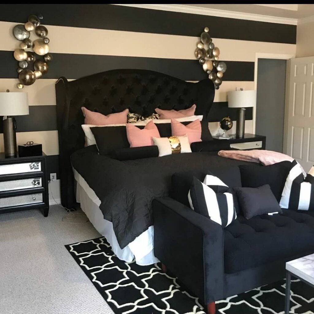 Quarto com parede listrada em preto e branco, cabeceira capitonê em veludo e cama posta com almofadas rosa