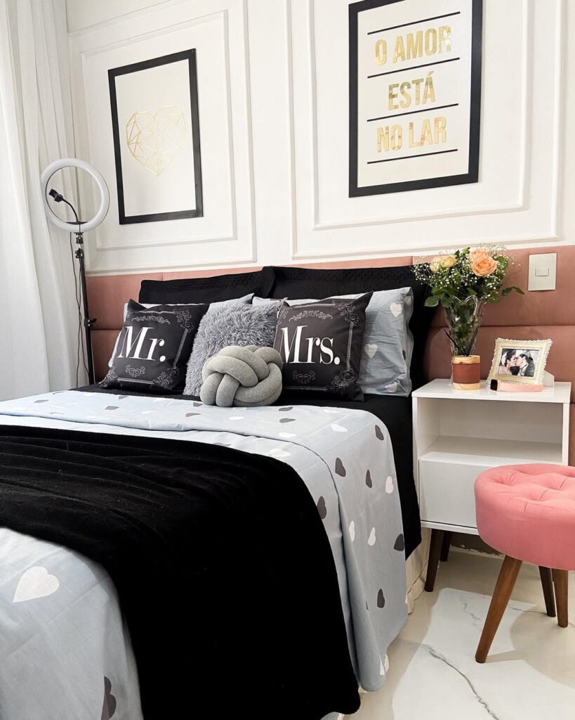 Quarto branco com cabeceira modular rosa, mesa de cabeceira branca e cama posta com colcha cinza e corações