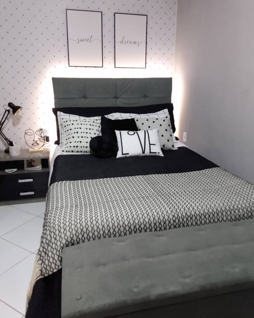 Quarto com papel de parede branco com bolinhas oretas, cabeceira cinza e cama posta em branco, preto e cinza
