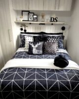 Quarto com cabeceira branca em lambri, prateleira acima com quadrinhos e cama posta com várias almofadas escuras