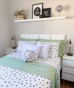 Cama posta verde e branco, cabeceira branca e prateleira suspensa acima com enfeites