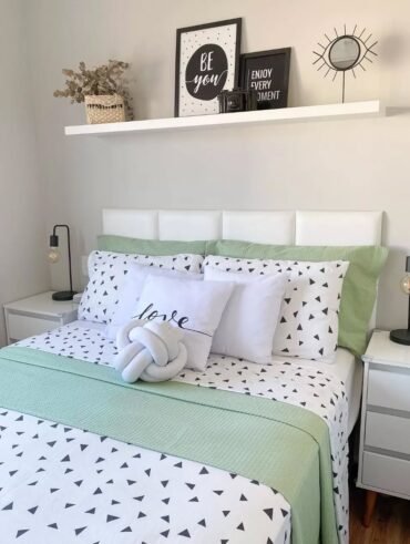 Cama posta verde e branco, cabeceira branca e prateleira suspensa acima com enfeites