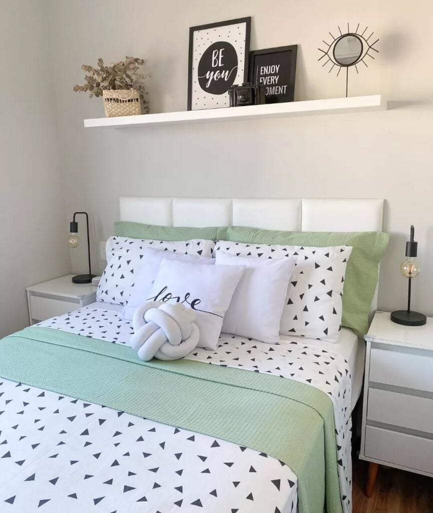 Cama posta verde e branco, cabeceira branca e prateleira suspensa acima com enfeites