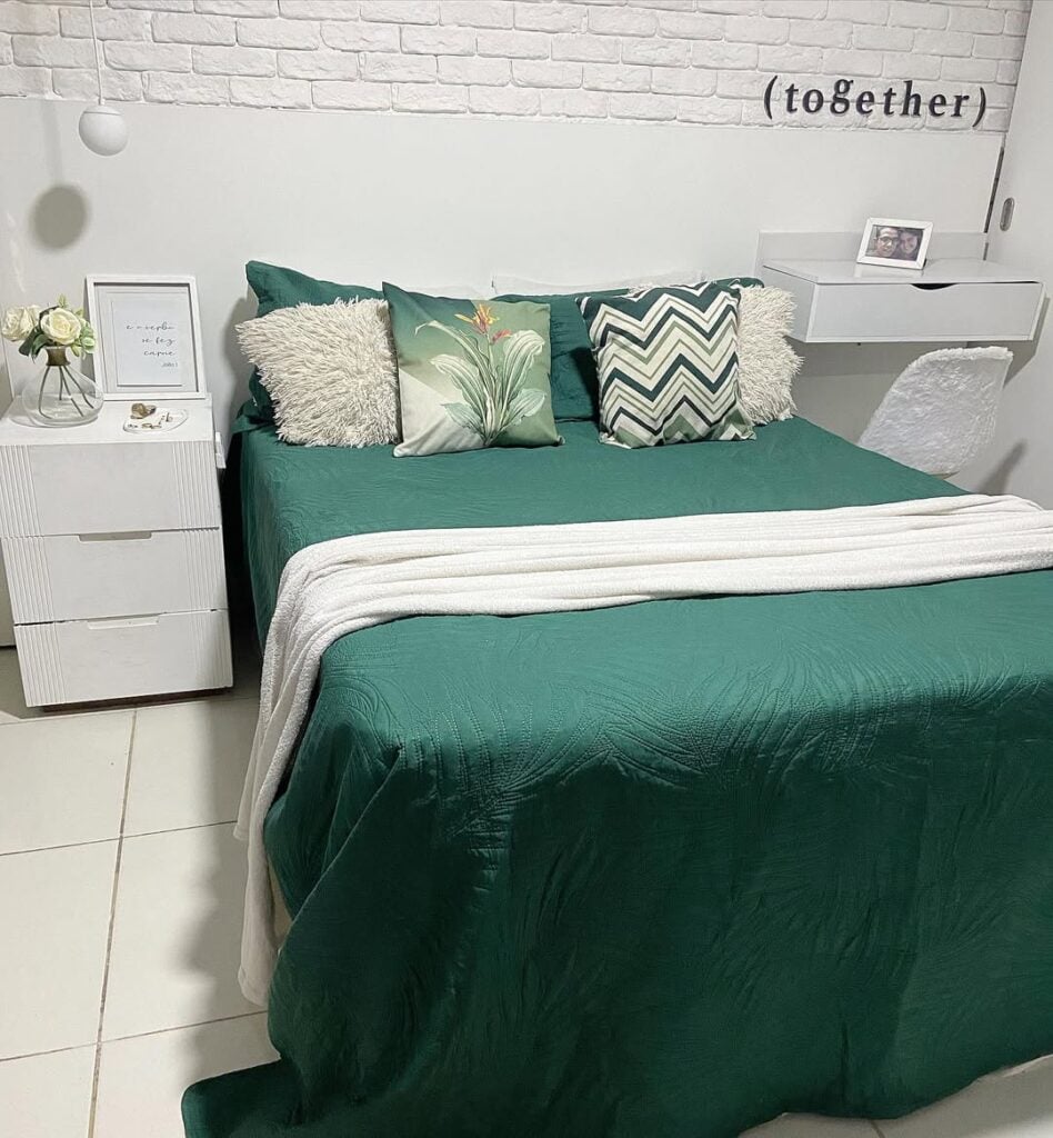Quarto branco com parede de tijolinhos, mesa de cabeceira com gavetas e cama posta verde